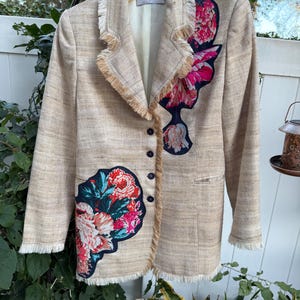 May include: Beige blazer with floral appliqué and fringe trim. The blazer features a textured fabric, black buttons, and the text "LA DIFFERENCE" on the label. The floral design includes pink, red, and teal colors.
