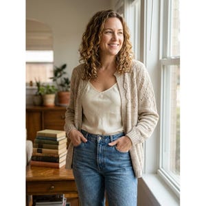 May include: A beige open-front knit cardigan with a textured diamond pattern on the sleeves and front panels, worn over a cream-colored camisole and blue denim jeans. The cardigan features ribbed cuffs and a ribbed hemline with a buttonless design.