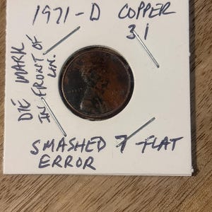 May include: A 1971-D copper penny with a die mark error, labeled "Smashed 7 Flat Error." The coin is mounted in a white card with handwritten notes. The card also has the text "COPPER 31".