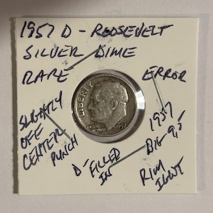 May include: A silver 1957 D Roosevelt dime, described as rare, with handwritten annotations noting an error and a slightly off-centre punch. The coin is in a protective holder with further handwritten details.