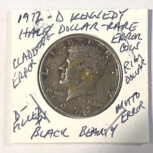 Puede incluir: Una moneda de medio dólar Kennedy de 1972, etiquetada como una moneda de error rara. La moneda plateada presenta un retrato de Kennedy. Notas manuscritas en la tarjeta indican varios errores y la frase "Black Beauty."