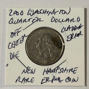 May include: A 2000 Washington Quarter Dollar coin, labeled as an off-center die error, is displayed in a protective holder. The holder is inscribed with handwritten notes indicating it is a rare New Hampshire error coin.