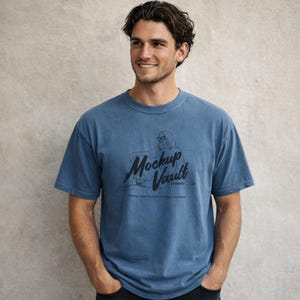 May include: A blue t-shirt with the text "Mockup Vault Studio" and a graphic of a person wearing glasses. The shirt is a solid color and has a crew neck. The text at the bottom of the graphic reads "Premium T-shirt Mockups For You & Designers."