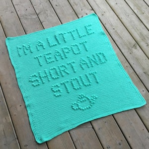 Könnte beinhalten: Eine türkisfarbene gehäkelte Babydecke mit dem Text "My Little Teapot Short and Stout" in erhabenen Buchstaben.