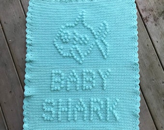 May include: A light blue crocheted baby blanket with a white crocheted flower design and the name "Avery" written in white crochet.