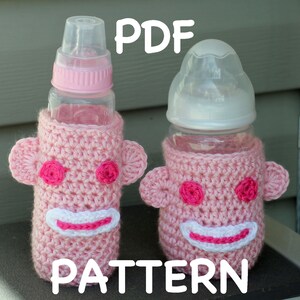 May include: PDF pattern for crocheting pink monkey bottle covers. The covers feature pink and white yarn with a smiling monkey face.