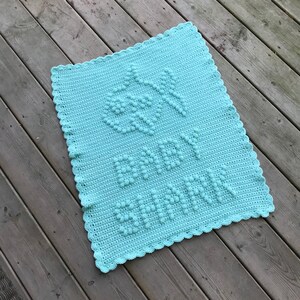 May include: A light blue crocheted baby blanket with a raised stitch pattern that spells out "Baby" in the center.