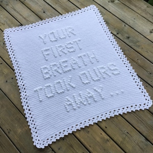 May include: White crocheted baby blanket with a scalloped border. The blanket features the text "YOUR FIRST BREATH TOOK OUR HEART AWAY" in raised lettering.