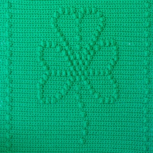 May include: A green crocheted square with a four-leaf clover design in the center.