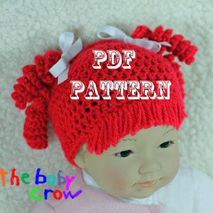 May include: A red crocheted baby hat with two white bows and pigtails. The hat has a "PDF PATTERN" text overlay. The text "The Baby Crow" is written in rainbow colors below the hat.