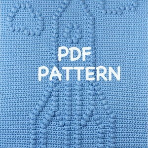 Op de afbeelding: Een blauwe gehaakte deken met een patroon van twee harten. De tekst "PDF PATTERN" staat in wit op de deken.