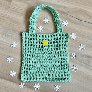 May include: A light green, crocheted tote bag with a yellow star applique. The bag has a rectangular shape with a handle and an open weave design. White snowflake decorations are scattered around the bag.