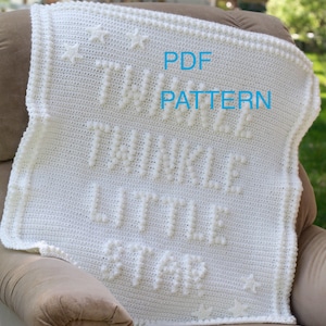 Peut inclure: Une couverture bébé en crochet blanc avec le texte "Twinkle Little Star" en points relief. La couverture a une bordure de perles blanches et des étoiles dans les coins. Le texte "PDF PATTERN" est écrit en bleu sur la couverture.