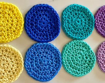 May include: Eight crocheted coasters in various colors, including yellow, blue, green, and purple. The coasters are circular and have a textured design.