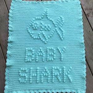 May include: A light blue crocheted baby blanket with a scalloped border and the name "Baby Savannah" written in raised stitches.