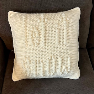 May include: A white crocheted cushion with a textured design. The cushion is made with a chunky yarn and has a simple, modern look.