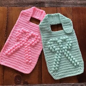 May include: Two crocheted bibs with a heart design. One bib is pink and the other is light blue.