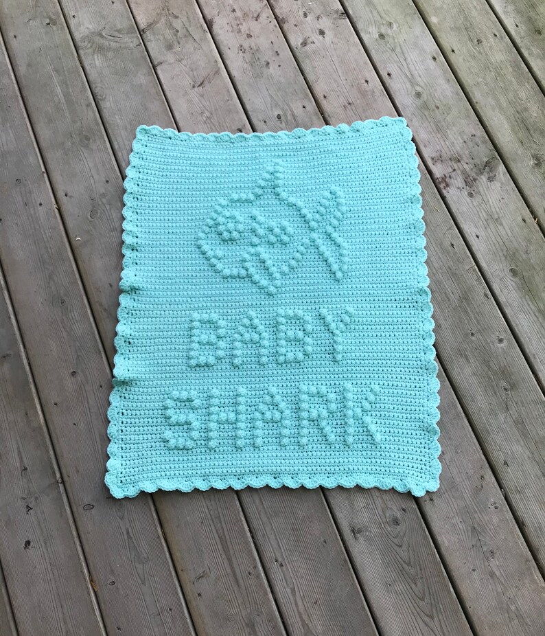 May include: A light blue crocheted baby blanket with a white crocheted border. The blanket has a raised design of leaves and the word "remarkable" in the center.