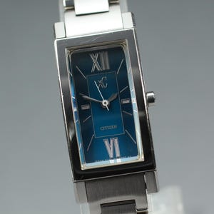 Könnte beinhalten: Rechteckige Citizen-Uhr mit silberfarbenem Metallarmband und Gehäuse. Das Zifferblatt der Uhr ist tief türkis mit silbernen römischen Ziffern und Zeigern. Auf dem Zifferblatt steht "Citizen".