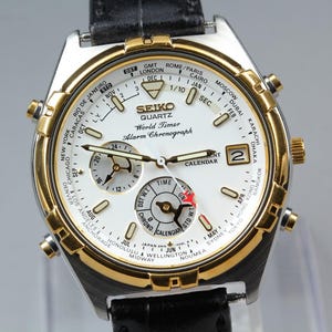 May include: A Seiko Quartz World Timer Alarm Chronograph watch with a white face, gold-tone bezel, and black leather strap. Features include multiple dials, a calendar, and world time indicators. The watch displays the time in various cities.