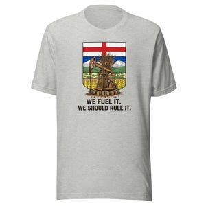 May include: Light grey t-shirt with a graphic featuring a shield design. The shield includes a red cross, an oil pump, wheat, and the text "WE FUEL IT. WE SHOULD RULE IT."