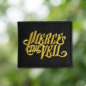May include: A black square patch with the words "Pierce the Veil" embroidered in gold script. The patch has a black border and is likely made of fabric. The background is a blurred green and yellow.