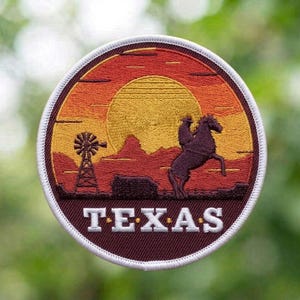 May include: A circular embroidered patch featuring a sunset landscape with a yellow sun, orange sky, and dark red terrain. The design includes a silhouette of a windmill and a person riding a horse. The word TEXAS is stitched in white capital letters.