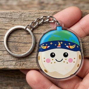 May include: A clear acrylic keychain featuring a smiling cartoon character with a blue and green globe-shaped hat and a navy blue headband with gold accents. The keychain has a silver chain and ring.