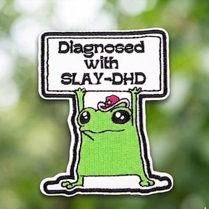 May include: A white ceramic mug with a black handle and the text "But First, Coffee" in a bold, black font. The mug is set against a blurred background, suggesting a cozy setting. The mug appears to be approximately 4 inches tall.