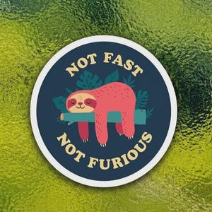 May include: A round sticker with a navy blue background and a white border. The sticker features a cartoon sloth resting on a branch, with the words "NOT FAST NOT FURIOUS" in yellow text.