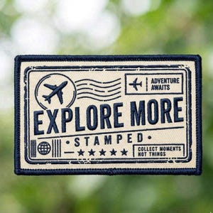 May include: A rectangular patch with a cream background and navy blue border. The patch features an airplane graphic, the words "EXPLORE MORE STAMPED", and the phrase "ADVENTURE AWAITS". The patch also includes a globe graphic and stars.