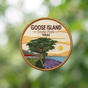 May include: A circular embroidered patch featuring a landscape scene of Goose Island State Park, Texas. The design includes a large green tree, a yellow sun, blue water, and a red-roofed building, with the text GOOSE ISLAND State Park TEXAS.