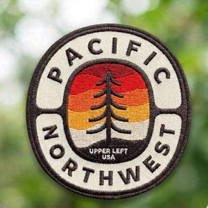 May include: Circular patch with the words "PACIFIC NORTHWEST" in black lettering around the edge. The center features a tree silhouette against a sunset gradient of red, orange, and yellow. The text "UPPER LEFT USA" is below the tree.