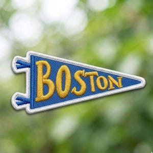 May include: Embroidered pennant patch in blue with the word "BOSTON" in gold lettering. The patch has a white border and blue accents, resembling a miniature flag. Ideal for jackets, bags, or other fabric items.