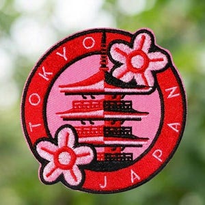 May include: Embroidered patch with the words "TOKYO JAPAN" in red around a pink circle. The patch features a pagoda and two pink flowers. The pagoda is split vertically, with red on the left and black on the right.