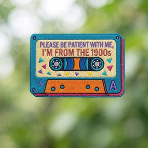 May include: Embroidered patch in the shape of a cassette tape. The patch is teal, orange, and beige with the text "PLEASE BE PATIENT WITH ME, I'M FROM THE 1900s". The design includes geometric shapes and the letter "A".