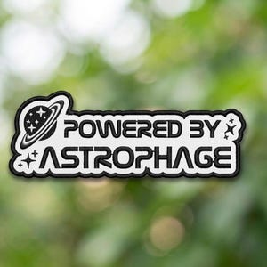 May include: Embroidered patch with the text "POWERED BY ASTROPHAGE" in black on a white background. The patch features a planet with stars and a black border. The patch is designed for clothing or accessories.