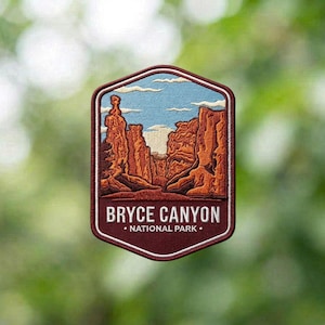 May include: A hexagonal embroidered patch featuring a landscape of orange and brown rock formations under a light blue sky with white clouds. The lower section is a dark red border with the white text BRYCE CANYON NATIONAL PARK.