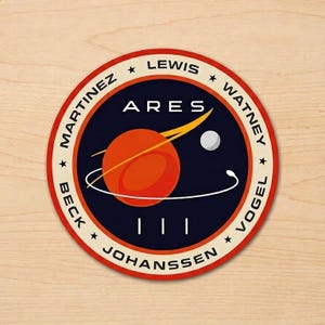 May include: A round sticker with a space-themed design. The sticker features a red and white border, with the word "ARES" in white text. The design includes a planet, a moon, and the names of the crew members.