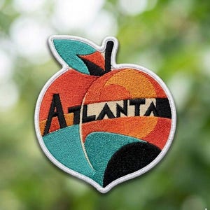 May include: Embroidered patch in the shape of a peach, featuring the word "ATLANTA" in black capital letters. The peach design incorporates orange, teal, and black geometric shapes. The patch has a white border and a green leaf.