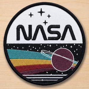May include: Embroidered NASA patch featuring the NASA logo in black on a white background. Below the logo is a colorful design of a planet with rings and a rainbow-colored arc. The patch is circular with a black border.
