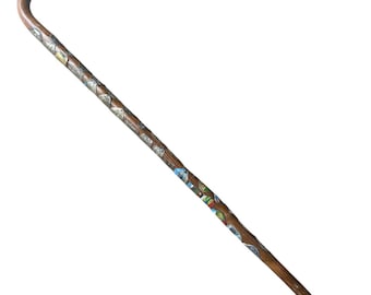 Puede incluir: Un bastón de madera marrón con un mango curvo. El eje está decorado con coloridas baldosas de mosaico y detalles metálicos plateados. El bastón tiene una punta negra.