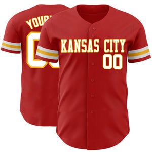 May include: A red baseball jersey with the words "KANSAS CITY" and the number "00" in white with a gold outline. The sleeves have gold and white stripes. The back of the jersey has the word "YOUR" and the number "00".