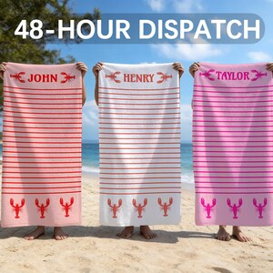 May include: Three rectangular beach towels featuring horizontal stripes and lobster motifs. The left towel is coral with red stripes, the center is white with red stripes, and the right is pink with dark pink stripes. Each towel displays a name.