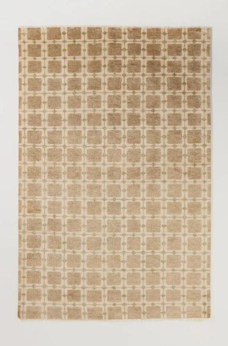 May include: A rectangular rug with a repeating geometric pattern. The rug features a beige background with a grid of squares in varying shades of brown and tan. The design is symmetrical and covers the entire surface.