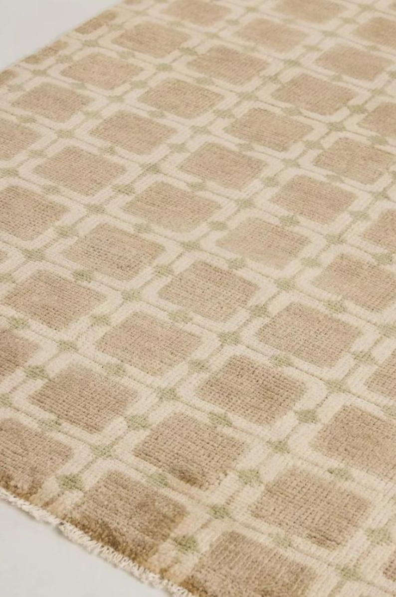 May include: A beige rug with a repeating geometric pattern of squares and diamonds. The squares are a darker beige color, outlined in a lighter beige, and the diamonds are a light green color.