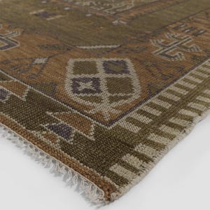 May include: Close-up of a corner of a distressed, patterned rug. The rug features a mix of olive green, brown, and beige tones with geometric and floral designs. The edge has a fringe detail, adding texture to the piece.