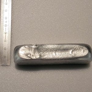 Op de afbeelding: Een zilverkleurige metalen staaf met een getextureerd oppervlak, ongeveer 7.6 cm breed en 15.2 cm lang, naast een metalen liniaal. De staaf heeft afgeronde randen en lijkt massief.