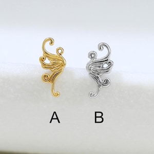 May include: Two small metal ear cuffs featuring an intricate swirling filigree design. Option A is finished in a bright gold tone, while option B is finished in a polished silver tone. Both pieces are labeled with the letters A and B respectively.