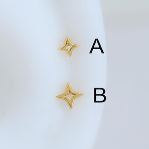 Puede incluir: Dos pendientes de botón dorados en forma de estrella. Un pendiente está etiquetado como "A" y el otro como "B". Los pendientes están sobre un fondo blanco.